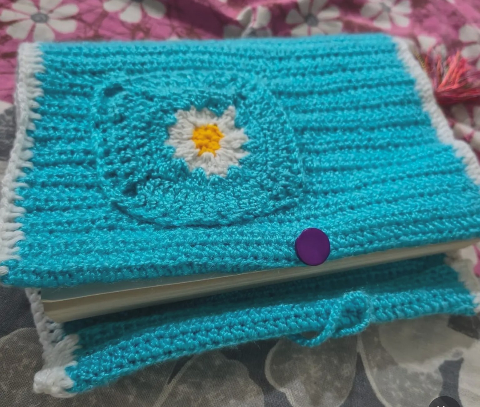 Handmade crochet notebook cover with turquoise weave, daisy granny square, and purple button